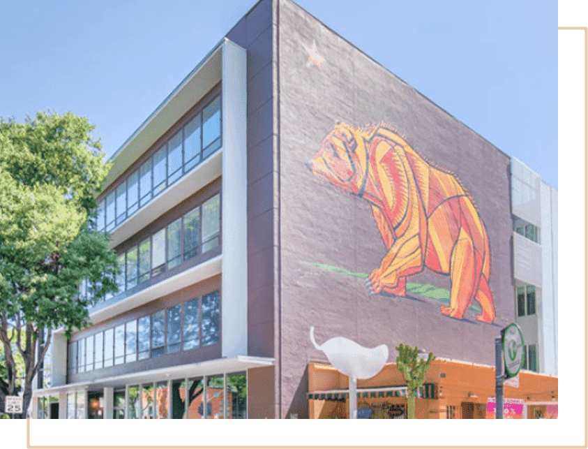 A three-story office building with a colorful mural of a bear on one wall and rows of tall windows on the other. 